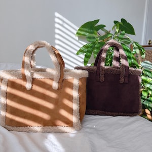 Puede incluir: Dos bolsos tote con exterior de ante sintético y un ribete esponjoso de color crema. Un bolso es de color marrón claro, el otro es de color burdeos intenso. Ambos tienen asas a juego.
