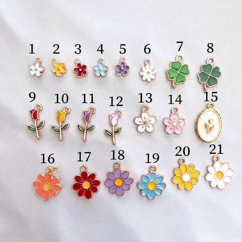 May include: A collection of twenty-one metal charms featuring various flower and clover designs in colorful enamel. Each charm is numbered from 1 to 21 and includes a small loop at the top for attachment. The designs include daisies, tulips, and clovers.