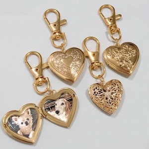 May include: Four gold-toned heart-shaped lockets attached to lobster claw clasps. One locket is open, revealing two photographs of dogs. Another locket features an intricate filigree cutout design, while the remaining two display embossed floral and heart patterns.