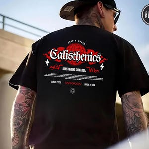 May include: A black t-shirt featuring a red globe graphic with the text Calisthenics, Grip & Grind, Mastering Control, and Since 2026. The design includes flame accents, lightning bolts, and small text blocks printed on the back of the garment.