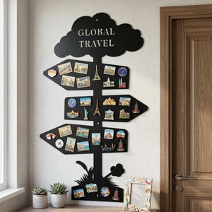Può includere: Decorazione murale in metallo nero a forma di albero con tre segnali direzionali. Il cartello recita "GLOBAL TRAVEL" e contiene calamite a tema viaggio. Due piante grasse in vaso e una foto incorniciata sono sul tavolo sottostante.