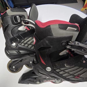 May include: Pair of black and gray inline skates with red accents. The skates feature a mesh design, adjustable straps, and four wheels each. The boots have a high-top design with a padded interior for comfort. The wheels are a translucent gray color.