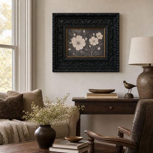 May include: A framed wall art piece featuring a botanical illustration of white flowers on a dark background, encased in a wide, ornate black frame with intricate carved details and a thin gold inner border, mounted on a neutral-colored wall.