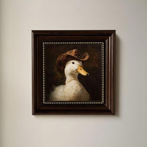 May include: A framed painting of a white duck wearing a brown cowboy hat. The duck has a yellow beak and is set against a dark background. The frame is dark brown with a dotted border.