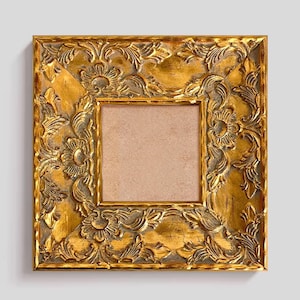 Puede incluir: Marco de fotos cuadrado dorado y ornamentado con intrincadas tallas de flores y hojas. El marco tiene un acabado envejecido y antiguo, con un respaldo de color neutro. Diseñado para una fotografía o obra de arte cuadrada.