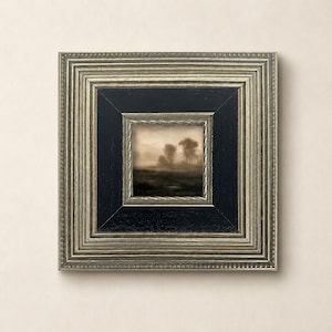 May include: A square framed artwork featuring a sepia-toned landscape of trees in a misty field. The frame has a multi-layered design with a wide, textured silver outer border, a smooth black inner section, and a thin, twisted silver inner trim.