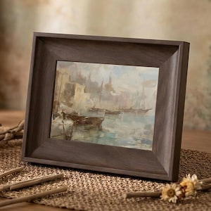 Może przedstawiać: Oprawiony obraz olejny przedstawiający łodzie w porcie. Dzieło sztuki jest osadzone w ciemnobrązowej drewnianej ramie. Obraz przedstawia stonowane odcienie niebieskiego, beżu i brązu, tworząc spokojną scenę nadmorską. Rama jest prostokątna.