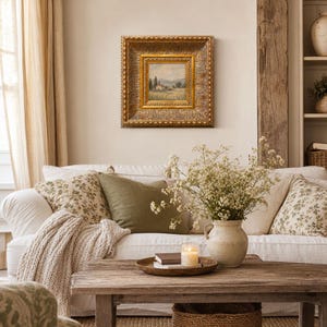 Könnte beinhalten: Ein gemütliches Wohnzimmer mit einem weißen Sofa, das mit floralen und olivgrünen Kissen geschmückt ist. Ein gerahmtes Landschaftsgemälde hängt darüber. Ein Holztisch zeigt eine Kerze, Bücher und eine Vase mit Blumen.