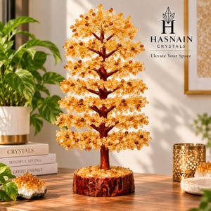 May include: A decorative tree sculpture featuring a dark brown trunk and base with numerous branches adorned with small, translucent yellow and amber-colored crystal beads. The text HASNAIN CRYSTALS Elevate Your Space is visible in the upper right.