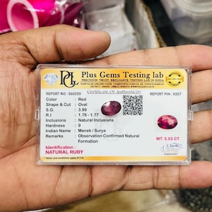 May include: A rectangular plastic case containing a certificate of authenticity for a natural ruby. The certificate displays the Plus Gems Testing lab logo, a QR code, and technical specifications including a weight of 5.53 CT and oval shape.