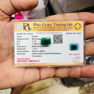 May include: A rectangular natural emerald gemstone with a green hue, presented in a clear plastic case alongside a Plus Gems Testing lab certificate of authenticity. The certificate lists the weight as 4.48 CT and includes a QR code and signature.