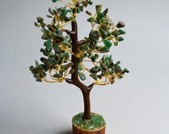 May include: A decorative tree sculpture with a brown trunk and branches, adorned with green gemstone leaves. The tree sits in a small wooden base, and the leaves are attached with gold wire.