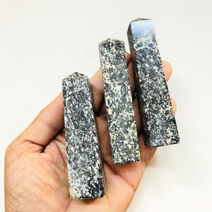 May include: Three rectangular, polished stone obelisks with a speckled black and white pattern. The obelisks are held in a hand against a white background. Each obelisk has a flat top.