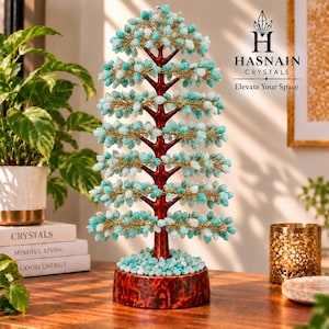 Könnte beinhalten: Eine dekorative Baumskulptur mit einem dunkelroten Stamm und Ästen, die mit zahlreichen kleinen hellblauen und weißen Kristallsplittern verziert sind. Der Baum steht auf einem runden, dunkelroten Sockel, der mit passenden Kristallsteinen bedeckt ist.