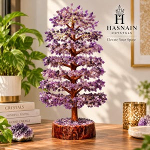 May include: A decorative tree sculpture featuring numerous small purple amethyst crystal chips attached to thin wire branches, supported by a brown trunk and a circular wooden base covered in amethyst stones, with the text Hasnain Crystals.