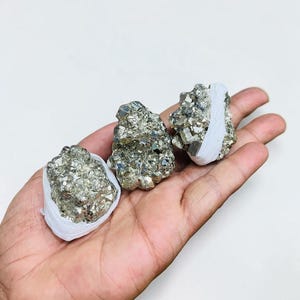 May include: A white ceramic mug with a black handle and the text "But First, Coffee" in a black, handwritten-style font. The mug is on a white surface.