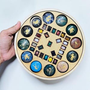 May include: A round wooden game board with a variety of colorful gemstones and zodiac symbols. The board features a central square with small stones and a circular outer ring with larger, round stones. The zodiac symbols are gold-colored.