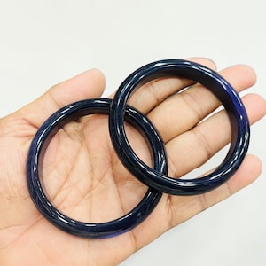 May include: Two circular bangle bracelets with a smooth, polished finish. The bracelets are a deep, translucent navy blue color with subtle, darker linear patterns visible throughout the material, creating a consistent and uniform appearance.