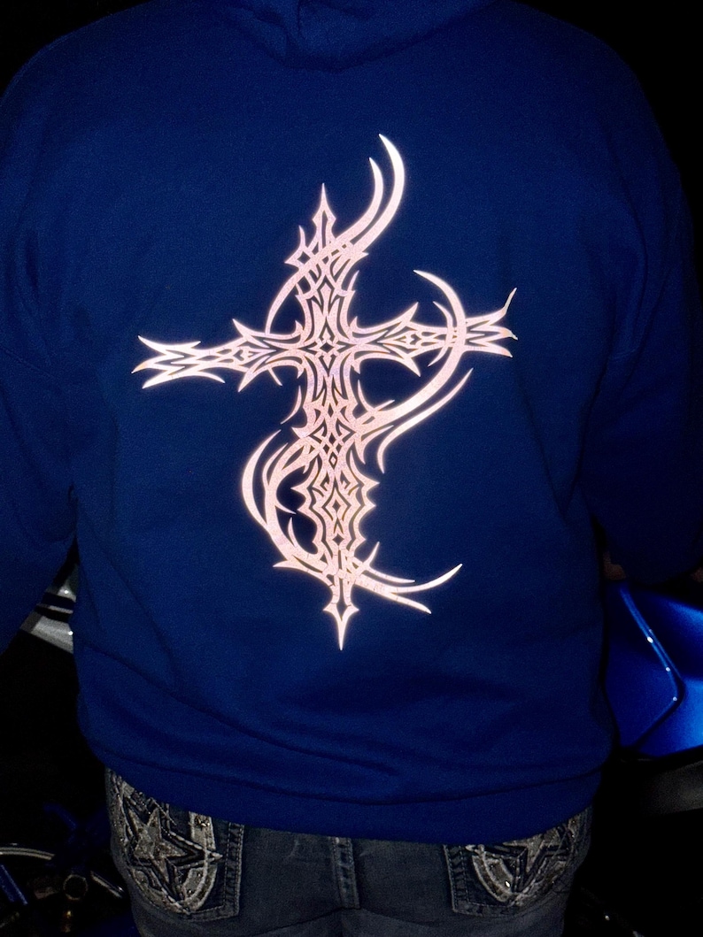 Pu&ograve; includere: Una felpa con cappuccio blu navy con un grande disegno a croce ornato sul retro. La croce &egrave; di colore rosa chiaro e presenta un motivo dettagliato di ispirazione tribale. La felpa ha un cappuccio e maniche lunghe.