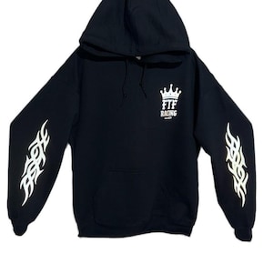 Pu&ograve; includere: Felpa con cappuccio nera con disegni di fiamme bianche sulle maniche e un logo a corona bianca con la scritta "FTF RACING". La felpa ha una tasca frontale e un cappuccio con coulisse.