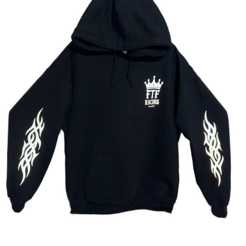 Pu&ograve; includere: Felpa con cappuccio nera con disegni di fiamme bianche sulle maniche e un logo a corona bianca con la scritta "FTF RACING". La felpa ha una tasca frontale e un cappuccio con coulisse.
