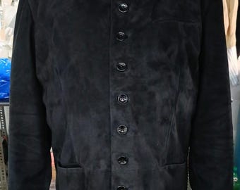 Puede incluir: Chaqueta de ante negra con cuello alto y cierre de botones. La chaqueta tiene un corte entallado, dos bolsillos delanteros y mangas largas. Los botones son negros y la chaqueta parece estar hecha de un material suave y texturizado.