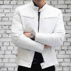 May include: A white leather jacket with a stand-up collar and quilted shoulder and sleeve detailing. The jacket features two zipped pockets on the chest and a silver zip closure. The model is wearing a watch.