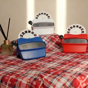 Könnte beinhalten: Drei View-Master im Vintage-Stil in Rot, Weiß und Blau stehen auf einer rot-weiß karierten Oberfläche. Jeder Betrachter hat eine schwarze Kurbel und eine kreisförmige Folie mit kleinen Bildern. Eine Diffusorflasche mit schwarzen Stäbchen ist ebenfalls vorhanden.