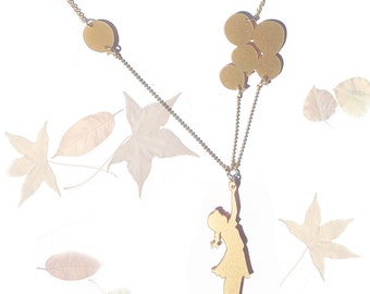 Op de afbeelding: Gouden ketting met een silhouet van een meisje dat ballonnen vasthoudt. De ketting heeft een kettinghanger in de vorm van een cirkel en een groep kleinere cirkelhangers.