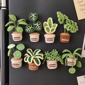 May include: Eight crochet plant magnets arranged in two rows. Each plant features green leaves in a small beige or brown pot with a brown tag labeled Handmade. The plants vary in leaf shape, including round, pointed, and textured foliage designs.