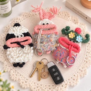 May include: Three crochet key pouches featuring whimsical character designs with wide pink mouths and metal key rings. One pouch is black and white, one is multicoloured with pink yarn tassels, and one is pink and green with small flower accents.
