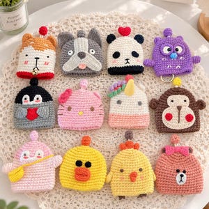 May include: A collection of twelve small, crocheted animal-themed pouches in various colours including orange, grey, white, purple, black, pink, yellow, and brown. Each pouch features embroidered facial details, small decorative toppers, and unique character designs.