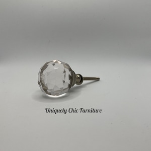 May include: A clear glass cabinet knob with a faceted design and a silver metal stem.