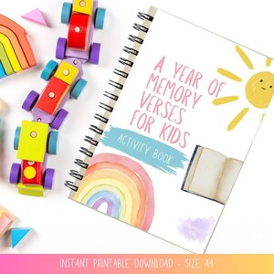 Pode incluir: Um livro de atividades com espiral intitulado "A Year of Memory Verses for Kids", com uma ilustração de arco-íris e sol. Carros de brinquedo de madeira coloridos, um empilhador de arco-íris e outros brinquedos de madeira estão espalhados ao redor do livro.