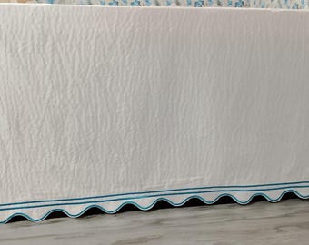 May include: White bed skirt with a textured surface and a scalloped edge. The edge is trimmed with a double line of teal blue stitching. The bed skirt is a simple, elegant design.