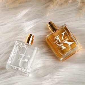 Peut inclure: Deux flacons de parfum en verre avec vaporisateurs dorés. L'un est transparent avec des motifs floraux blancs et le texte "Happy 55th Mum". L'autre est rempli de liquide ambré et porte le nom "Kristina" et un motif floral.