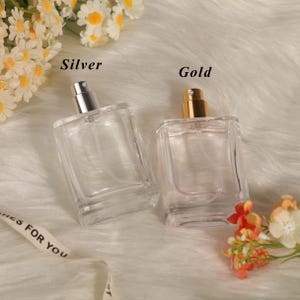 May include: Two rectangular clear glass perfume bottles with spray nozzles. One bottle features a silver-colored cap and the text Silver, while the other has a gold-colored cap and the text Gold. Both bottles are empty and have clear plastic tubes.