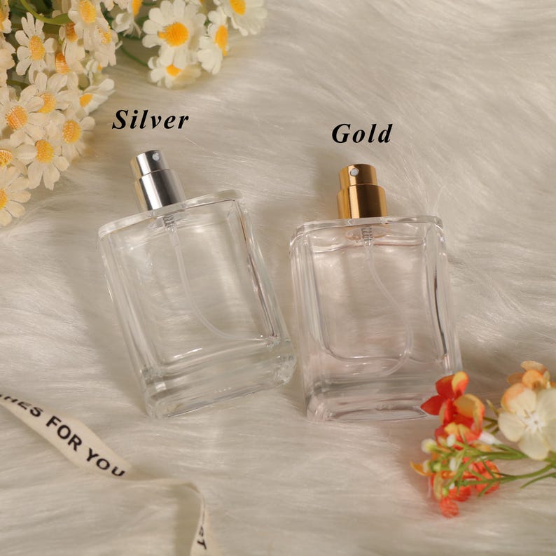 May include: Two rectangular clear glass perfume bottles with spray nozzles. One bottle features a silver-colored cap and the text Silver, while the other has a gold-colored cap and the text Gold. Both bottles are empty and have clear plastic tubes.