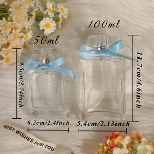 May include: Two clear glass perfume bottles with spray pumps and light blue ribbon bows. The smaller bottle is 50ml, 3.74 inches tall, and 2.4 inches wide. The larger bottle is 100ml, 4.6 inches tall, and 2.13 inches wide. Text reads BEST WISHES FOR YOU.