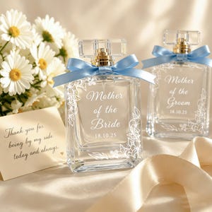 May include: Two clear glass perfume bottles with light blue ribbons tied around the necks. One bottle is etched with Mother of the Bride 18.10.25 and the other with Mother of the Groom 18.10.25, both featuring white floral line art designs.
