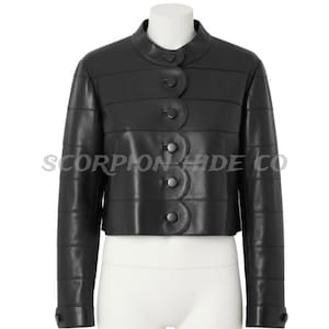 Puede incluir: Chaqueta de cuero negra con cuello mandarín y cierre de botones festoneados. La chaqueta presenta detalles de costura horizontales. El texto "SCORPION HIDE CO" está impreso en la parte delantera.