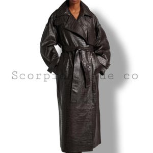 Puede incluir: Un abrigo tipo trench de color marrón oscuro con textura de piel de cocodrilo. El abrigo tiene un cuello ancho, un cinturón y cierres de botones. Las mangas son largas y el abrigo llega hasta los tobillos. El texto "Scorpion hide co" está impreso en el abrigo.