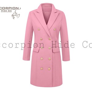 Puede incluir: Un blazer rosa de manga larga y doble botonadura con botones dorados. El blazer tiene un cuello con solapas clásico y dos bolsillos delanteros. El texto "scorpion Hide Co" está impreso en la parte superior izquierda e inferior central de la imagen.