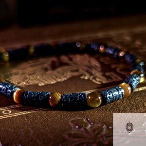 May include: A bracelet with alternating dark grey textured beads and round, golden-brown tiger eye beads. The bracelet is presented on a brown surface, highlighting the natural colours and textures of the materials.