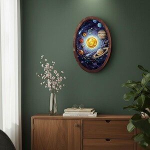 Peut inclure: Une œuvre d'art murale de forme ovale représentant une peinture à l'huile vibrante du système solaire avec un soleil central, diverses planètes dont Saturne avec ses anneaux et de la poussière cosmique, dans un cadre en bois brun.