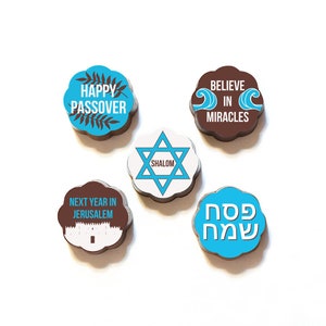 Puede incluir: Cinco monedas de chocolate con diseños azules y blancos. Las monedas muestran las frases "Feliz Pascua", "Cree en milagros", "Shalom", "El próximo año en Jerusalén" y "Pesaj Sameaj".
