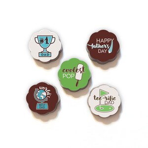 以下が含まれることがあります： 父の日のメッセージが異なる、花の形をしたチョコレート5個。チョコレートは白地に茶色、緑、青のアクセントが施されています。メッセージには、「#1パパ」、「世界で一番のパパ」、「最高のパパ」、「父の日おめでとう」、「最高の父」などがあります。