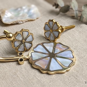 May include: A set of gold-toned metal hardware including a curved wall hook and two flower-shaped knobs, each inlaid with iridescent white mother-of-pearl segments. The text THE ARTISAN'S SHELL is printed in the bottom right corner of the image.
