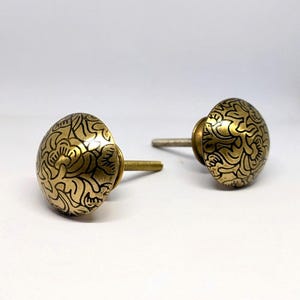 Peut inclure: Deux boutons de meuble en laiton avec un motif floral. Les boutons ont une forme arrondie et une finition dorée avec des détails noirs. Les vis sont argentées et dorées. Ces boutons décoratifs conviennent aux meubles et à la décoration intérieure.