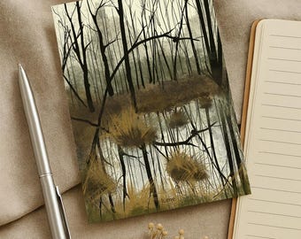 May include: A landscape art print featuring a forest scene with tall, bare trees and a muted color palette of browns, greens, and grays. A silver pen and a notepad with lined pages are next to the print. The word "lume" is visible on the print.